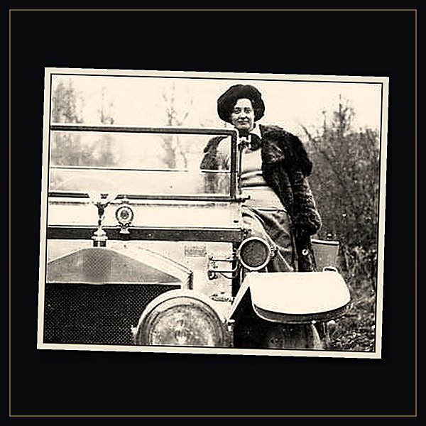 A period photograph of Eleanor Thornton, the woman behind the flying lady, in a fur coat standing beside a vintage motor car with a small silver figure on its bonnet.