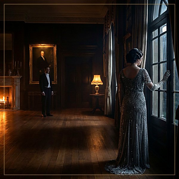 A woman in a beaded evening gown stands alone at a tall window in a candlelit Edwardian drawing room while a man in evening dress watches from across the floor.