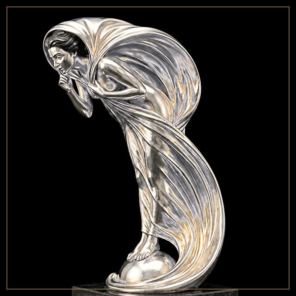 The Whisper by Charles Sykes. A silver statuette of a woman leaning into the wind with a finger laid across her lips, standing on an orb on a marble plinth.